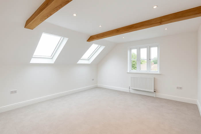 Islington Conversions & Renovation – bright loft room with skylight windows, exposed beam, and neutral interior finish